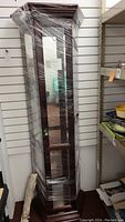 Full view of curio cabinet wrapped in plastic showing wooden frame and glass panels