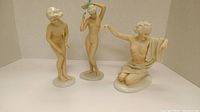 Three porcelain nude figurines displayed together on white surface