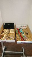 Two trays holding assorted vintage jewelry including necklaces, bracelets, watches, pins, patches, and a Lancome pouch