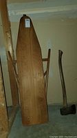 Front view of wooden ironing board and axe showing ironing board top surface and full axe