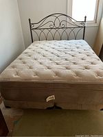 Front view of mattress on box spring, showing tufted pillow top surface and metal bed frame headboard