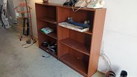 Two medium brown wood-tone bookcases side by side, showing multiple shelves with some items placed on them, in a garage or storage area.