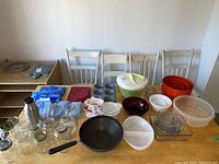 View of entire kitchenware lot on table showing jars, bowls, bakeware, cookware, and containers illustrating assortment and condition