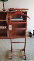 Front view of wooden suit butler valet stand showing hanger, trouser bar, and wheels at the base.