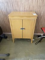 Front view of the small painted wood cabinet showing two doors with round metal knobs and decorative top molding.
