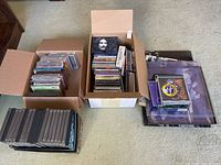 Box with several CDs and DVDs including a George Harrison CD on top, and other assorted CDs/DVDs beside it