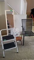 Photo showing folding step stool, wall mirror, outdoor chair, wooden stool and oscillating fan grouped together.