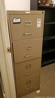 Full height view of beige metal four drawer filing cabinet in office setting.