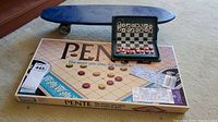 Wide shot with blue skateboard in the background, Pente board game box, two ticket stubs on board, and magnetic chess game open showing pieces.