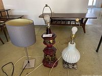 Three table lamps placed together showing two lamps without shades and one with a textured gray shade.