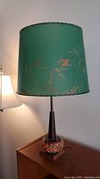 Full view of lamp showing green fiberglass shade and painted ceramic base on wooden platform