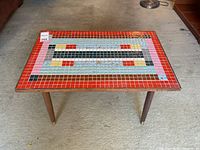 Front view of the rectangular coffee table showing the colorful mosaic tile top with geometric patterns featuring red, pink, light blue, yellow, black, and gray tiles.