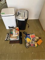 Photo showing entire lot including Fellowes paper shredder, white pedal trash bin, and assorted office supplies arranged on floor.