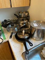 Wide angle photo of various pots, pans, lids, and large stockpot on kitchen counter.