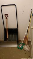 Photo showing the full lot of cleaning and snow removal tools against a wall, including snow scoop, shovel, broom, and mops.