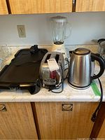 Full view of the lot showing all small appliances including blender, kettle, toaster, hot plate, and electric griddle on a kitchen counter.