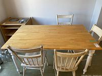 Rectangular kitchen table with light wood top and white turned legs, accompanied by four vintage painted spindle back chairs with white paint, showing wear.