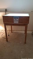 Wooden table supporting a rectangular lightbox with glowing white translucent top surface, plugged in and turned on.