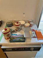 Photo of the full lot on kitchen counter showing decorative tins, ceramic bowls, baking pans, shortbread tin, and utensils.
