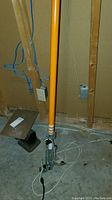 Full view of the orange handle and metal cutting head resting vertically on the floor against a wall.