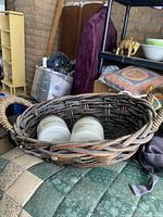 Dark brown woven basket with rope handles containing two white candles in glass jars.