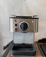 Front view of Cuisinart espresso machine showing control dial, power and heating lights, and missing grate on drip tray.