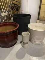 Red, black, white, and small beige indoor planters grouped together on floor near a stair case