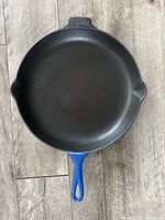 Top-down view showing black cooking surface with signs of wear and blue enamel handle and sides.