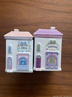 Front and side view of Lenox porcelain containers labeled Dill and Thyme with pastel colored roofs and detailed floral designs