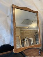 Full view of the smaller wooden framed mirror showing curved top and bottom edges, used condition with visible wear on wood.