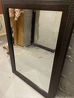Mirror with dark textured frame shown leaning against wall
