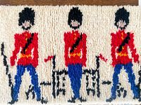 Close-up image showing three Queen's Guards in red uniforms, blue pants, and tall black bearskin hats, hooked into a white background fabric.