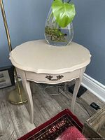 Beige finished side table shown with decorative vase on top, highlighting its scalloped edge and curved legs.