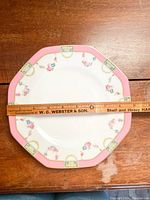 Hexagonal Royal Doulton plate with pink border, gold accents, and floral decorations, shown flat with ruler for size reference.