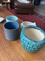 Four blue ceramic planters including pig-shaped, leaf texture, fern pattern, and geometric floral designs.
