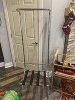 Full view of the chrome suitcase rack with integrated coat bar standing in front of white door.