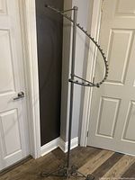 Overall view of the tall grey clothing rack placed near door, showing entire swirl arm and vertical pole.