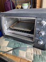 Front view of black toaster oven with glass door, metal rack and baking pan inside. Control knobs visible on the right.