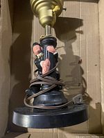View of lamp base with wrapped cord showing Charlie Chaplin figure leaning on lamp post on black circular base.