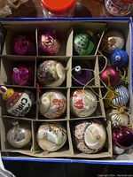 Top-down photo showing a divided box containing an assortment of vintage mercury glass and silk Christmas bulbs in various colors and designs.