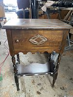 Front view of vintage tall parlour side table showing cupboard door with decorative metal applique and wooden knob. Turned spindle legs and lower magazine shelf visible.