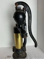 Full view of antique cast iron water pump with brass cylinder against white background