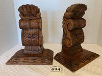 Front and side angled view of the pair of antique carved wooden corbels showing detailed carved scroll and floral design with a scalloped edge at the top.