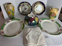 Full view of all items including the bowl, platters, vases, plates, and cloth napkins arranged on a white cloth background