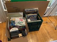 Overview of boxes and crate holding various art papers, cardboard, paints and art supplies.