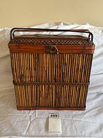Front view of bamboo basket showing vertical bamboo slats, front latch, and two handles on top folded down.
