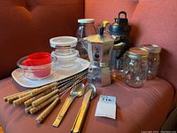 Full view of the kitchen lot including the Bialetti stove top espresso maker, fondue forks, mason jars, glass containers, spoons, cups, and white tray.