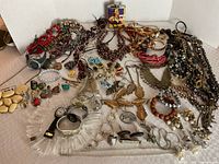 Wide shot showing full assortment of costume jewelry items including multiple necklaces, earrings, rings, bracelets, and watches.