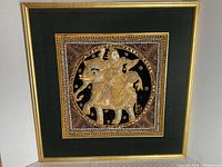 Framed embroidered artwork of a person riding an elephant with black velvet background and gold frame.