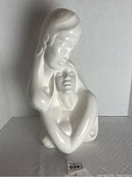 Front view of the glossy white ceramic figurine of two people embracing, showing overall form and posture.